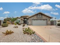 Charming stone home featuring desert landscaping, a spacious driveway, and a two-car garage under a sunny sky at 14458 W Powderhorn Dr, Surprise, AZ 85374