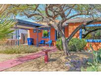 Charming orange home with blue trim, shaded seating area, and a vibrant desert-landscaped yard at 1454 E Flower St, Phoenix, AZ 85014