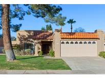 Charming home featuring a red tile roof, two-car garage, and a well-maintained front lawn with mature landscaping at 9088 E Winchcomb Dr, Scottsdale, AZ 85260