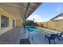 Relaxing pool area with a covered patio, stylish gray tile and two chairs for enjoying the outdoors at 2438 E Claire Dr, Phoenix, AZ 85032