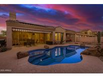 Inviting backyard pool with rock features, covered patio, and seating under a sunset sky at 9604 S 183Rd Dr, Goodyear, AZ 85338