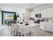 Modern white kitchen with an island, seating, stainless steel appliances, and stylish light fixtures at 23984 W Cocopah St, Buckeye, AZ 85326