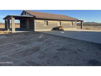 Side exterior view showcasing the concrete driveway that leads to the block constructed house with tile roof at 9600 S 393Rd Ave, Tonopah, AZ 85354
