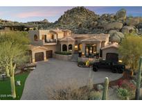 Luxurious Tuscan-style home with a circular driveway, grand staircase, and desert landscaping against a mountain backdrop at 10471 E White Feather Ln, Scottsdale, AZ 85262