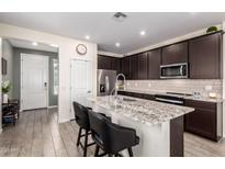 Modern kitchen featuring dark cabinets, stainless steel appliances, and a granite countertop island with seating at 17308 W Daley Ln, Surprise, AZ 85387