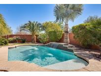 Sparkling pool features a waterfall and is surrounded by lush landscaping and mature palm trees at 15613 W Minnezona Ave, Goodyear, AZ 85395