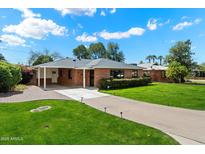 Charming brick home with well-manicured lawn and a long driveway leading to covered parking area at 1939 E Solano Dr, Phoenix, AZ 85016