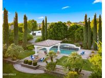 Aerial view of a backyard featuring a pool, spa, covered patio, outdoor fireplace, and lush landscaping at 2174 E Avenida Del Valle Ct, Gilbert, AZ 85298