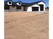 A white house with black trim and a black roof, showing a large garage and a spacious yard at 11142 E Copper Dust Trl, Florence, AZ 85132