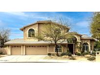 A tan stucco home has a three car garage and arched front entry, along with desert landscaping at 6828 E Evans Dr, Scottsdale, AZ 85254