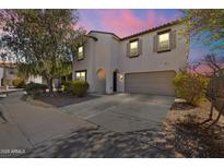 Two-story home featuring a desert-style landscape and a two car garage is awash in pink light from the setting sun at 17043 N Avelino Dr, Maricopa, AZ 85138