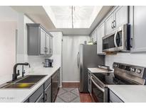 Galley kitchen features gray cabinets, stainless appliances, white countertops, tile backsplash and a stylish skylight at 3830 E Lakewood E Pkwy # 2042, Phoenix, AZ 85048