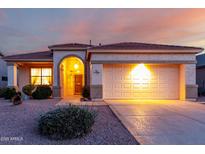 Charming single-story home with desert landscaping, arched entry, and warm exterior lighting at dusk at 17805 W Arizona Dr, Surprise, AZ 85374