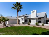 Charming single-story home with a well-manicured lawn, palm trees, and a bright white exterior at 10934 E Becker Ln, Scottsdale, AZ 85259