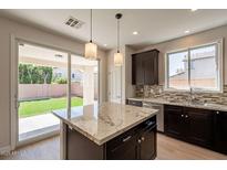 Stylish kitchen showcasing granite countertops, dark cabinets, stainless steel appliances, and access to backyard at 18123 W Lundberg St, Surprise, AZ 85388