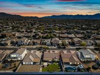 Expansive aerial view of a neighborhood showcasing a community with mountain views under a vibrant sunset at 5318 W Grenadine Rd, Laveen, AZ 85339