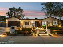 Charming home with warm exterior lighting, modern landscaping, a dark garage door and a stone walkway to the front door at 4316 N 86Th Pl, Scottsdale, AZ 85251