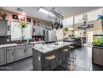 Bright kitchen featuring gray cabinets, granite countertops, and a pot rack above the kitchen island with bar stool seating at 44235 W Mcclelland Dr, Maricopa, AZ 85138