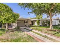 Charming single-story home featuring a well-maintained lawn and a brick-accented driveway leading to a covered carport at 302 E Orange Dr, Phoenix, AZ 85012