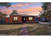 Charming red brick home featuring a well-maintained lawn and an inviting walkway during a colorful sunset at 2511 E Pinchot Ave, Phoenix, AZ 85016