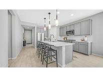 Modern kitchen with gray cabinets, stainless steel appliances, a spacious island with seating, and elegant pendant lighting at 13511 W Cassia Trl, Peoria, AZ 85383