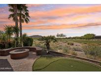 Inviting backyard with lush greenery, putting green, fire pit, and golf course views at 27926 N 130Th Ave, Peoria, AZ 85383