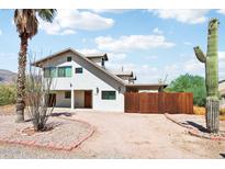 Two-story white house with desert landscaping, a gravel driveway, and a wooden fence, all under a partly cloudy sky at 5599 S Alameda Rd, Gold Canyon, AZ 85118