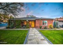 Charming red brick home with a bright yellow door, lush green lawn, and eye-catching desert landscaping at 1402 E Granada Rd, Phoenix, AZ 85006