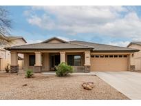 Charming home featuring a two-car garage, covered porch with stone accents, and desert landscaping at 16187 W Gibson Ln, Goodyear, AZ 85338