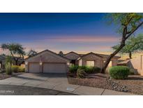 Charming single-story home featuring a three-car garage, desert landscaping, and flag at sunset at 1620 W Nighthawk Way, Phoenix, AZ 85045