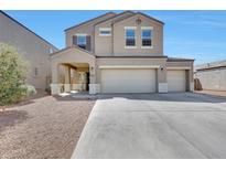 Two story home featuring a two-car garage, manicured landscaping, and a welcoming covered front porch at 30683 W Amelia Ave, Buckeye, AZ 85396