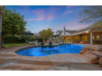 Inviting backyard pool area with a rock feature, lounge chairs, outdoor kitchen, and a covered patio for entertaining at 9015 E Altadena Ave, Scottsdale, AZ 85260