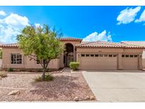 Tan home showcasing desert landscaping, a three-car garage, and a charming tiled roof under a bright blue sky at 1777 W Redfield Rd, Gilbert, AZ 85233
