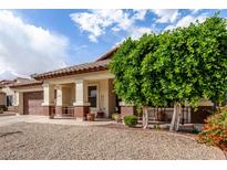 Attractive home showcasing a covered porch area with desert landscaping, mature trees, and a two-car garage at 15328 W Memory Ln, Surprise, AZ 85374