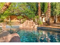 Inviting backyard pool featuring a charming rock waterfall, mature palm trees, and sparkling blue water at 4223 N St Elias --, Mesa, AZ 85215