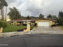 Charming single-story home featuring a well-manicured lawn, colorful flowerbeds, and a two-car garage on a cloudy day at 554 W Southern Hills Rd, Phoenix, AZ 85023