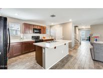 Well-lit kitchen featuring an island, modern appliances, wooden cabinets, and wood-look tile flooring at 16562 W Sierra St, Surprise, AZ 85388