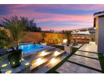 Inviting backyard with a pool, spa, outdoor kitchen, fire pit, and covered patio at dusk at 32268 N 133Rd Ln, Peoria, AZ 85383