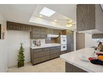 Well-lit kitchen with tile floors, a skylight, dark wood cabinets, and white countertops and breakfast bar at 11113 W Cameo Dr, Sun City, AZ 85351