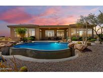 Desert home showcasing a luxurious backyard pool with rock features, set against a stunning sunset sky at 42145 N Fairgreen Ct, Anthem, AZ 85086