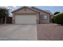 Tan single-story home with a spacious driveway and two-car garage, trimmed with stacked stone accents at 15351 W Port Royale Ln, Surprise, AZ 85379