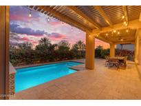 The backyard boasts a sparkling pool, covered patio with string lights, and a seating area, perfect for outdoor entertaining at 175 E Santa Lucia Ln, Queen Creek, AZ 85140