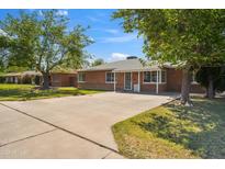 Charming brick home featuring a well-manicured lawn, mature trees, and a spacious driveway on a sunny day at 1529 W Rovey Ave, Phoenix, AZ 85015