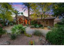 Stunning home featuring lush desert landscaping, a circular driveway, and stone accents under a colorful sunset sky at 11821 S Tuzigoot Ct, Phoenix, AZ 85044