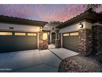 Stunning home exterior featuring a stone facade, two-car garage, and a charming gated entrance, all under a beautiful twilight sky at 19245 W Pasadena Ave, Litchfield Park, AZ 85340