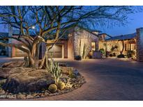 Elegant desert home with stone accents, lush landscaping and a circular driveway at twilight at 10057 E Blue Sky Dr, Scottsdale, AZ 85262