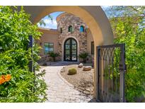 Charming home exterior features a stone tower, complemented by a brick walkway framed by mature desert landscaping and an arched gate at 37334 N Winding Wash Trl, Carefree, AZ 85377