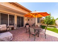 Relaxing back patio featuring a brick floor, comfortable seating, and an orange umbrella for shade at 22940 W Desert Bloom St, Buckeye, AZ 85326