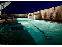 Inviting pool with small waterfall feature and desert landscaping, illuminated at night for a relaxing ambiance at 11934 S 181St Ave, Goodyear, AZ 85338