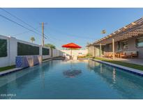 A backyard pool with a waterfall feature and an orange umbrella, surrounded by lounge chairs at 8522 E Virginia Ave, Scottsdale, AZ 85257